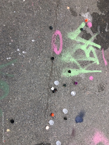 Discarded graffiti spray paint caps scattered on rough urban asphalt covered in street-art