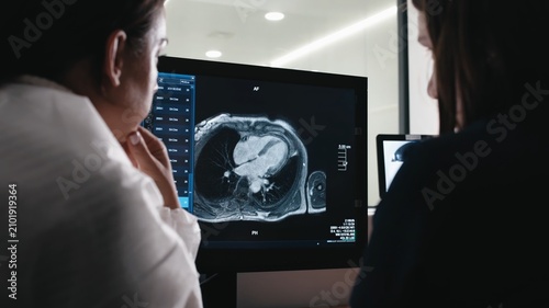 Clinical specialists reviewing cardiac MRI images on a diagnostic workstation during collaborative medical imaging workflow in a modern hospital