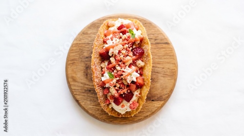 Gourmet langos bread topped with rich cream cheese diced beetroot and crispy onion crumbles served on a rustic round wooden board over white background with bright high key lighting and clean