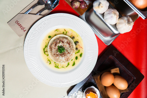 Konstfotografi Gourmet Delight: A perfectly plated dish, showcasing a delicate mousse, sits in a white ceramic bowl, surrounded by fresh ingredients like garlic, onions, and eggs, hinting at a culinary masterpiece