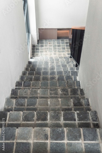 Quadro su tela Stone Stairway Descent: A textured stone staircase descends, its weathered grey blocks forming a compelling pattern, leading the eye downwards into the interior of a building
