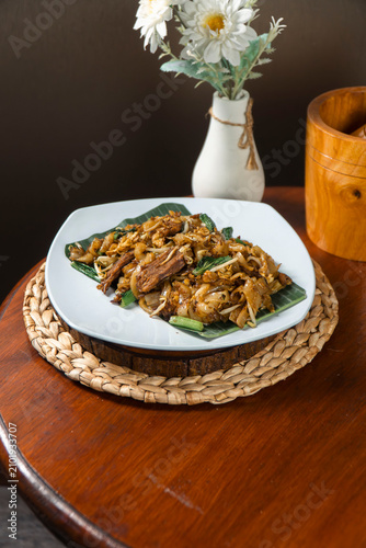 Canvastavla Savory Stir-Fried Noodles on Banana Leaf: A delicious plate of stir-fried noodles, topped with tender meat and fresh greens, rests on a banana leaf, ready to be savored