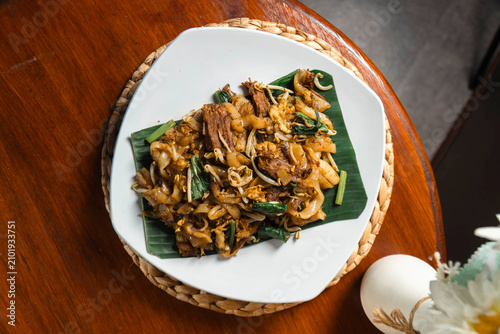 Fotografie Savory Stir-Fried Noodles: A vibrant plate of stir-fried noodles, showcasing tender meat and fresh vegetables, served on a banana leaf for an authentic culinary experience