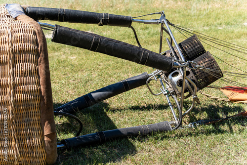 Close-up of a hot air balloon basket and burner system resting on a green grassy field before or after a flight. Professional equipment for aerostatic aviation close up.