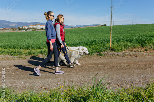 Two women walking a Maremma Sheepdog in the countryside