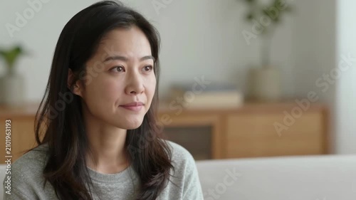 Smiling Asian Woman Sitting on Couch in Living Room with Indoor Plants
