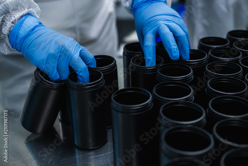 Close up of factory worker hands in blue gloves sorting black plastic bottles concept of pharmaceutical medicine packaging production line quality control