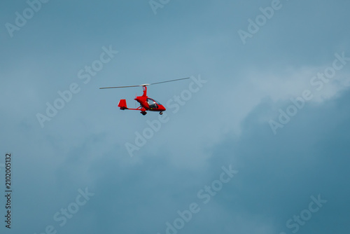 Small red helicopter flying in cloudy sky