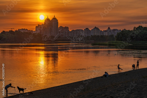 Beautiful golden hour sunset over Dnieper river in Kyiv with silhouettes of people and dogs on Obolon beach