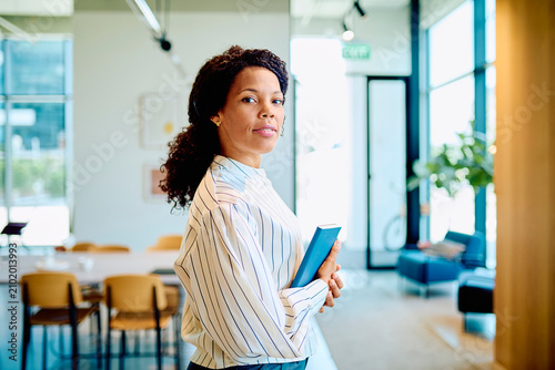 Obraz na plátně Confident Black businesswoman standing in a contemporary office setting, holding