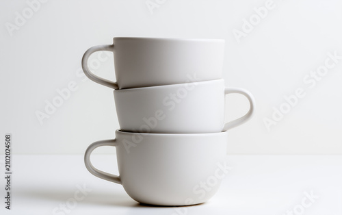 Three white porcelain coffee cups stacked on light surface, minimalist style, soft shadow, clean and modern kitchen decor