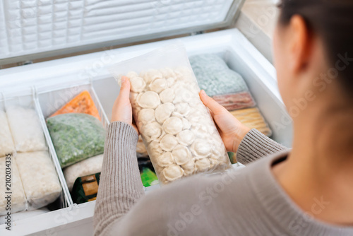 A person is holding a bag of light-colored, roundish food items inside an open refrigerator.