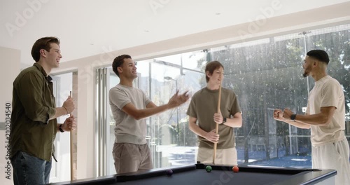 Diverse male friends playing pool by doors, cheering after shot, breaking rack, scattering balls