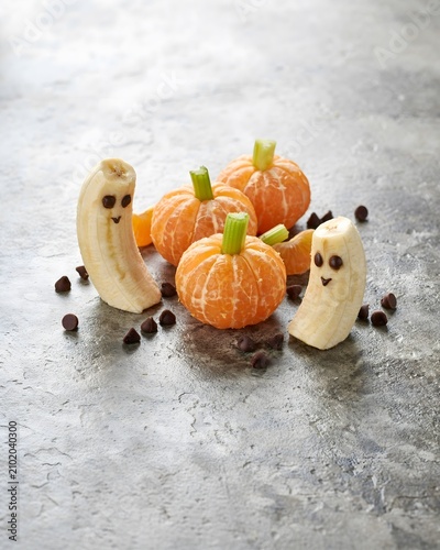Halloween fruit snacks cute banana ghosts and mandarin orange pumpkins on a marble surface