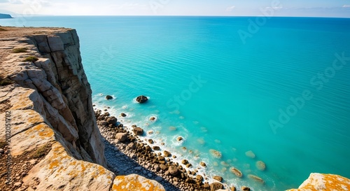 Stunning cliffside view over turquoise ocean with rocky beach and clear sky on sunny day.