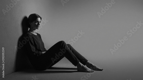 Woman sitting against the wall in a dark room with expression  