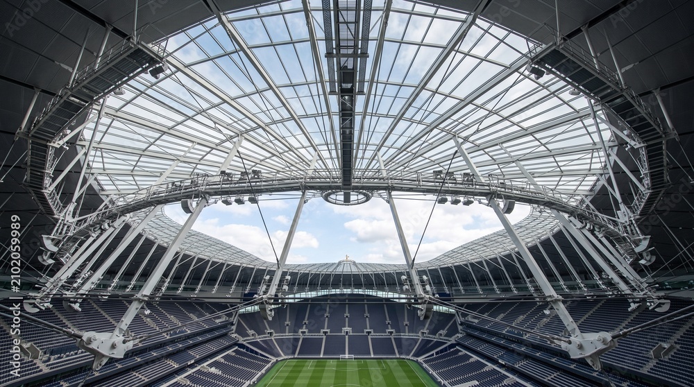 Fototapeta premium Wide angle view of a large stadium interior with a retractable glass roof, green grass pitch, and empty seating, architectural structure