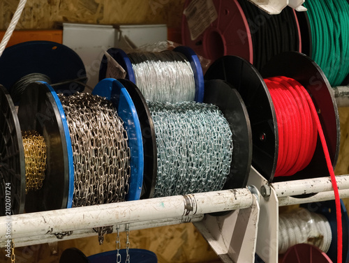 Assorted metal chains and rope bundles coiled on reels in a supermarket hardware aisle presenting strong construction materials for logistics and heavy duty use