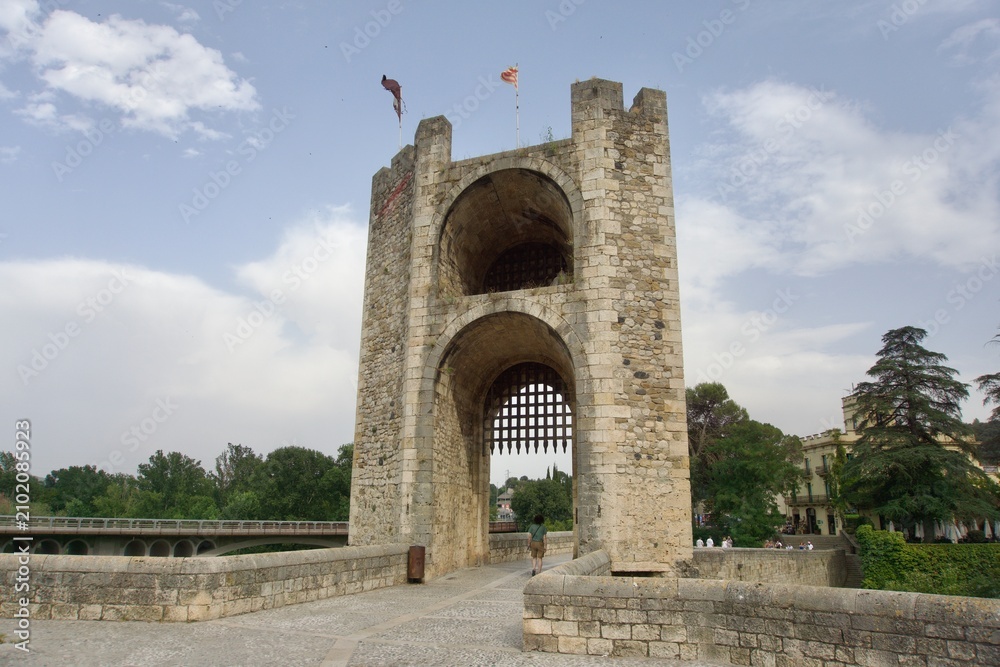 Obraz premium Besalu, Spain - June 16, 2026: Low-angle view of the fortified stone gate tower on the medieval Pont Vell (Old Bridge), with a portcullis visible beneath its arches, Girona province, Catalonia.