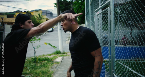 Slika na platnu Two Hispanic men argue intensely outside in street, shouting and pushing as emot