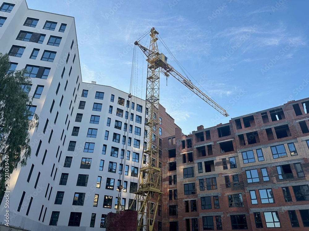Fototapeta premium Exterior of building and construction crane under blue sky, low angle view