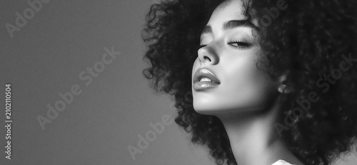 FINE ART SFUMATO PORTRAIT OF A BEAUTIFUL YOUNG BLACK WOMAN WITH NATURAL CURLY HAIR AND EYES CLOSED IN PEACEFUL EMOTION ON LIGHT GREY BACKGROUND WITH NEGATIVE SPACE