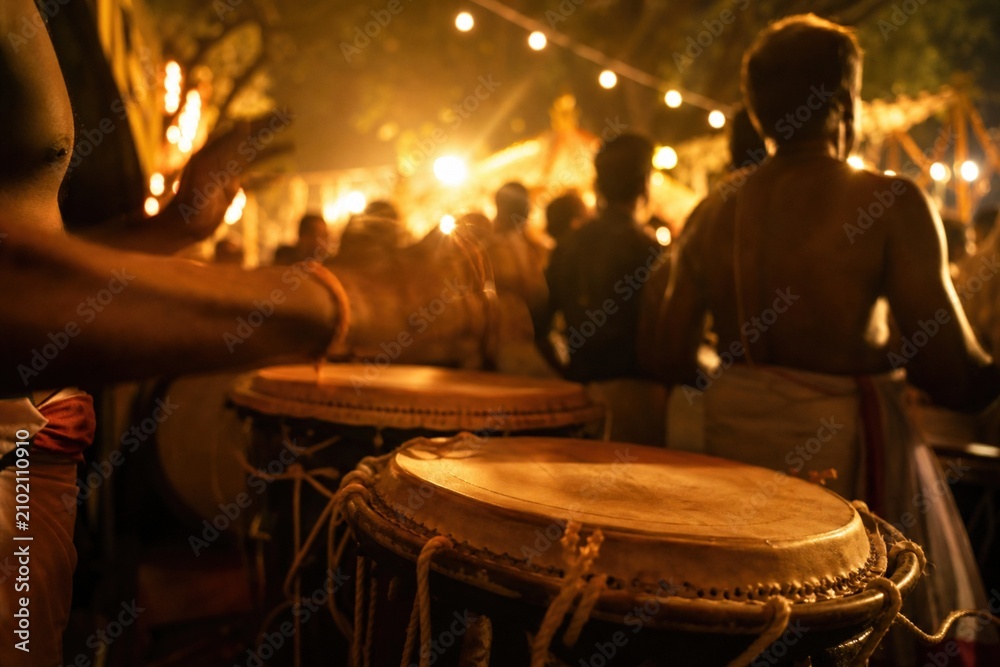 Fototapeta premium Traditional Indian percussionists playing chenda drums during a vibrant night festival celebration with warm glowing lights and a festive crowd
