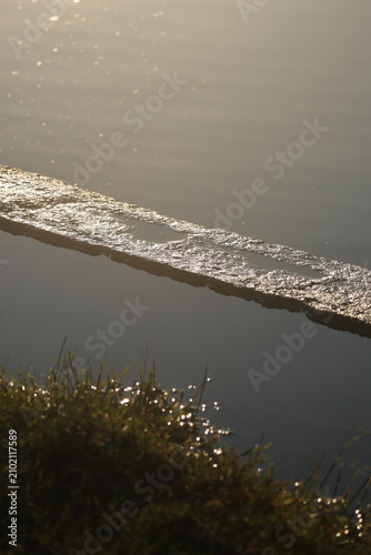 Bild auf Leinwand Backlit concrete shore edge glittering in golden light cutting diagonally across calm lake water at sunrise