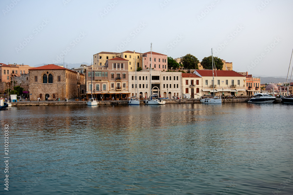Obraz premium Colourful Venetian houses line the waterfront of the old harbour of Chania with boats and reflections on the island of Crete in Greece, a popular travel destination.