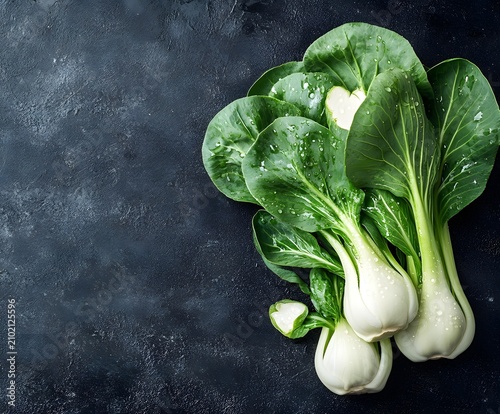 Fresh bok choy with water droplets on dark textured background viewed from above.