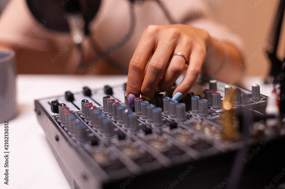 Fototapeta premium Content creator checks sound on a DJ mixer for a podcast, recording digital media during an online broadcast show, using a microphone setup for online media production.