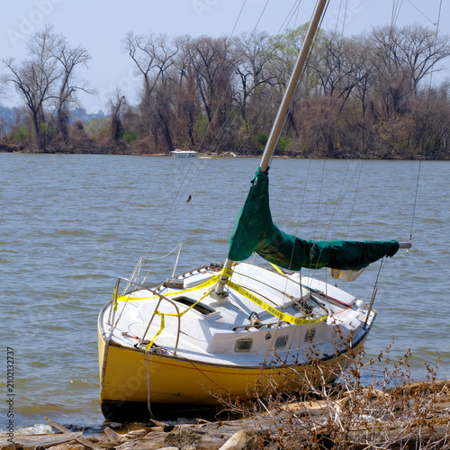 An abandoned sailboat run aground in the foreground and a partially submerged boat in the background