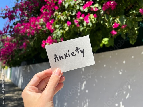 Anxiety -  card with text in the hand and pink flowers on background, mental health concept