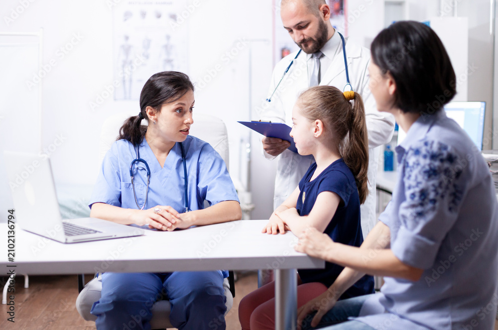 Fototapeta premium Nurse listens to a child during a hospital consultation while a doctor takes notes, supporting pediatric examination and treatment planning, keeping the focus on consultation, healthcare and the.