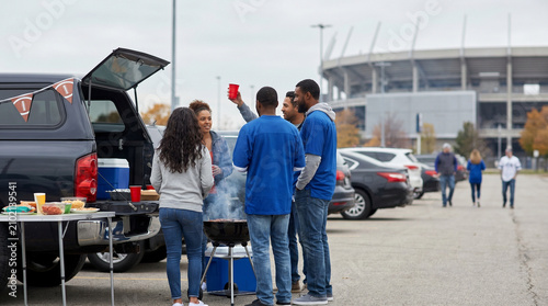 Group of friends enjoying a tailgate party outside stadium parking lot  