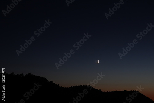 Obraz na płótnie Luna creciente brillante y estrella en el cielo nocturno sobre silueta de bosque al atardecer