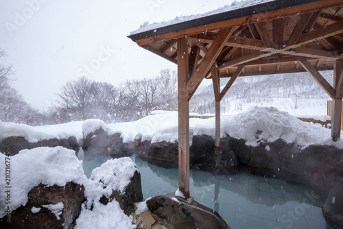 Snow-covered outdoor hot spring in Hokkaido with steaming water and mountain views during winter