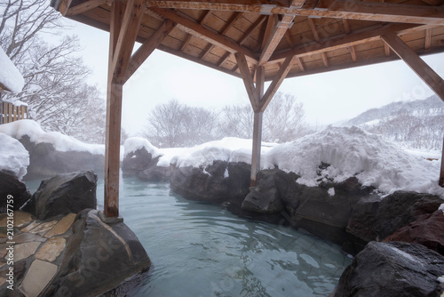 Snow-covered outdoor hot spring in Hokkaido with steaming blue thermal water and wooden pavilion