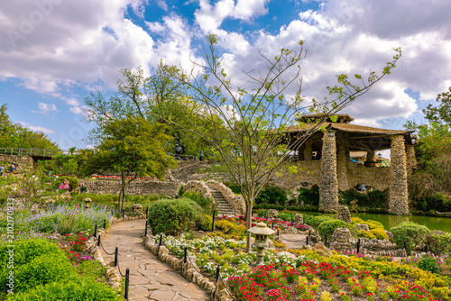 Stone walkway curving through colorful flower gardens past a traditional stone lantern toward the main pavilion at the Japanese Tea Garden.