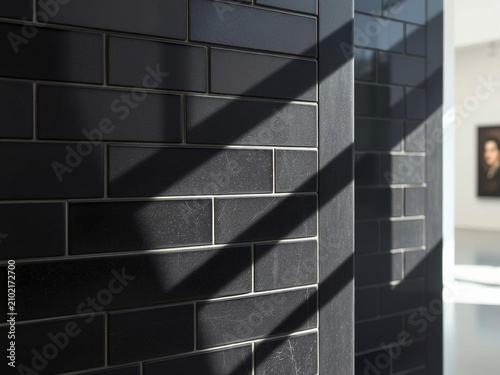 Abstract image of a modern black brick wall with strong diagonal shadows and bright sunlight creating a dramatic contrast, hinting at an interior space with a blurred portrait painting in the backgrou