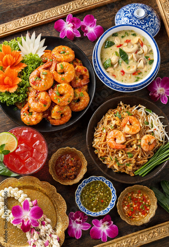 Authentic Thai cuisine flat lay featuring Pad Thai, spicy glazed shrimp, and coconut curry served on a wooden table with orchids