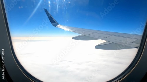 Airplane wing and clouds viewed from passenger window during flight