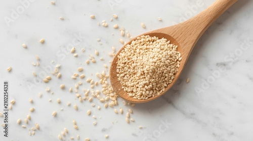Top view of healthy organic white sesame seeds in a wooden spoon on a white marble background