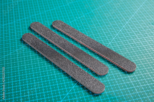 Konstfotografi Three gray emery nail files arranged diagonally on green cutting mat for manicur