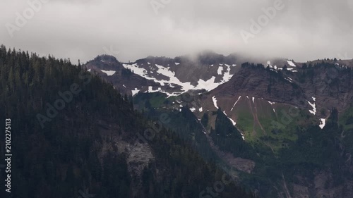 Aerial of Cascade Mountains peaks in Gifford Pinchot National Forest with patches of residual snow and low clouds