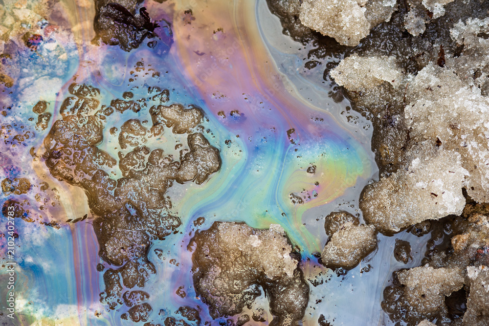 Obraz premium Iridescent sheen from oils and fuels on melting snow and puddles, spring thaw, environmental pollution