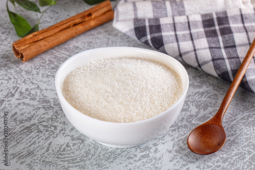 Foto White sugar crystals in bowl with wooden spoon and cinnamon sticks