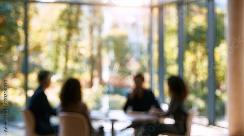 Blurred view of people in a meeting room with sunlight and greenery outside