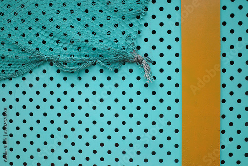 Vertical yellow color and Turquoise Fishing Net Draped Over Perforated Metal Wall Texture Background