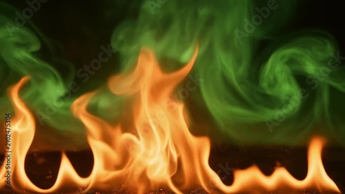 Mesmerizing dance of bright orange flames flickering intensely, merging with vibrant green smoke, creating captivating visual